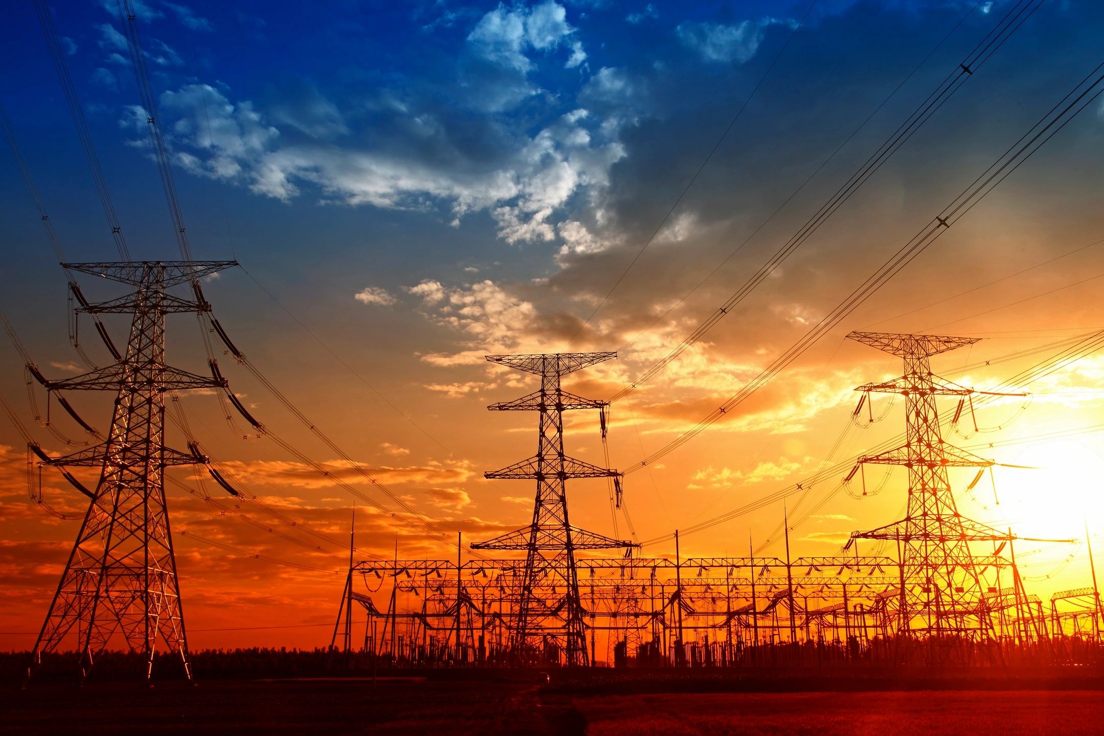 High voltage power lines and transmission towers at sunset generating electricity